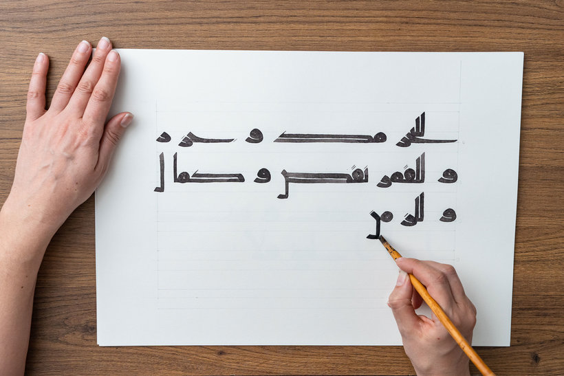 Calligrapher drawing Kufic forms at a wooden desk